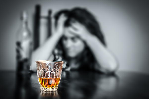 A woman in black and white struggling with alcohol in a glass in front of her